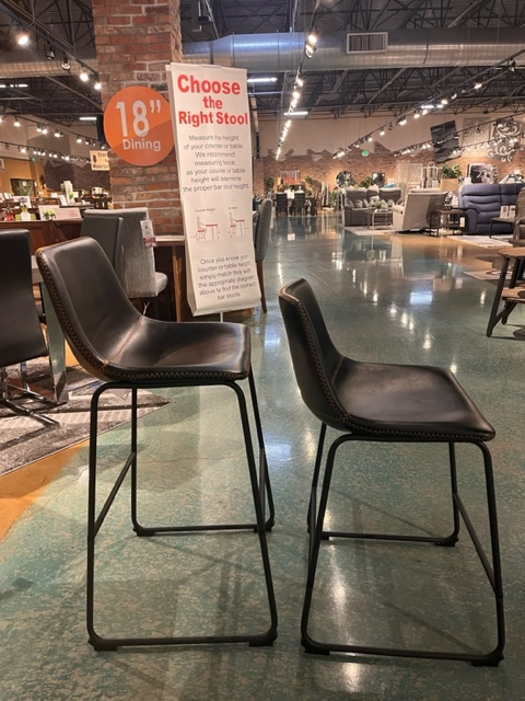 Two vintage black barstools with orange stitching, one at counter height and the other at bar height 